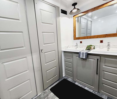 An interior view of a Lang restroom trailer with sink, vanity, mirror, and restroom stall doors.