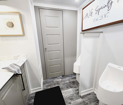 An interior view of a Lang Restroom Trailer Mens side with 2 urinals and sink vanity.