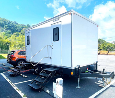 An exterior view of a Lang 2 Station Restroom trailer stationed at a campground parking lot.